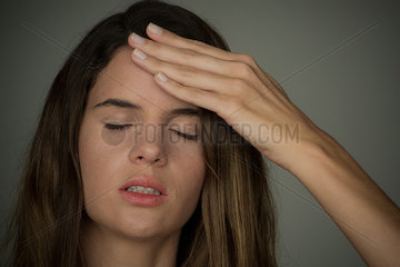 Young woman holding hand on forehead with eyes closed