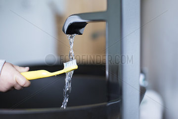 Child holding toothbrush under water faucet