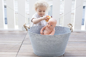 Little girl bathing baby doll in bucket outdoors