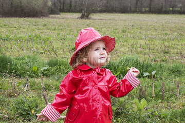 Little girl wearing rain gear playing in field