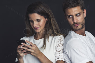 Man glaring over his shoulder as girlfriend uses smartphone