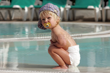 Pajara  ein kleines Kind in Windeln hockt an einem Swimmingpool