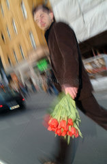 Berlin  Mann mit Tulpenstrauss ueberquert eine Strasse