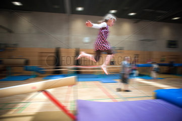 Berlin  Deutschland  blondes Maedchen springt von einem Schwebebalken in einer Turnhalle