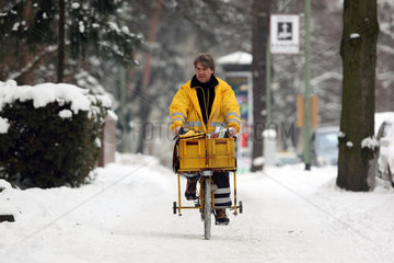 Berlin  Deutschland  Postbote der Post AG faehrt auf seinem Fahrrad einen schneebedeckten Gehweg entlang