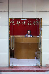 Peking  Frau sitzt in einem kleinen Buero am Empfangstresen