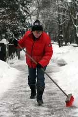 Neuenhagen  Deutschland  Frau fegt Schnee vom Gehweg