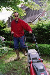 Mann beim Rasenmaehen in einem Garten