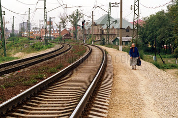 Alte Frau geht an einem Gleis entlang