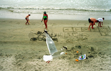Borkum  eine tieffliegende Moewe und eine spielende Familie am Strand