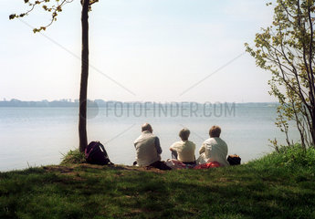 Eckernfoerde  drei Menschen sitzen am Ufer eines Binnensees