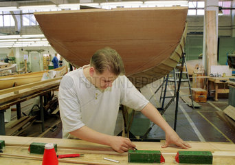 Berlin  ein Umschueler (Bootsbauer) bearbeitet eine Holzplanke