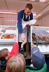 Deutschland  Fischhaendler reicht Kindern Aal auf dem Hamburger Fischmarkt
