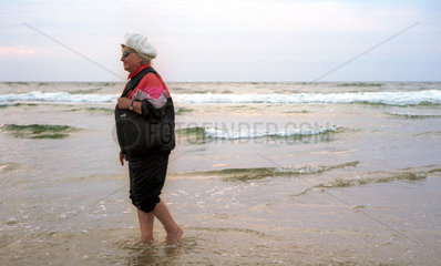 Miedzyzdroje  eine aeltere Frau geht barfuss im Wasser spazieren