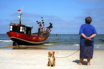 Miedzyzdroje  eine Urlauberin mit Hund beobachtet ein ablegendes Fischerboot