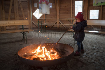 Berlin  Deutschland  kleines Maedchen stochert in einem Holzfeuer herhum