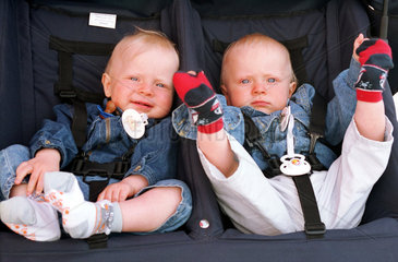 Einjaehrige Zwillinge sitzen in ihrem Kinderwagen