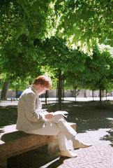 Berlin  Deutschland  lesende Frau im Sonnenlicht unter Baeumen