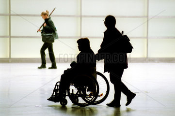 Silhouetten von einer Frau  die eine andere im Rollstuhl schiebt