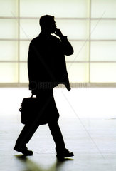 Silhouette eines telefonierenden Mannes mit Koffer