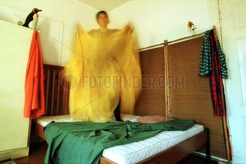 Hausarbeit: Frau mit Bettlaken auf einem Bett stehend