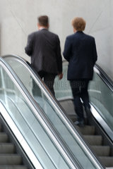 Zwei Maenner im Anzug auf einer Rolltreppe