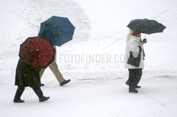Spaziergaenger mit Regenschirmen im Schnee