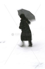 Spaziergaengerin mit einem Regenschirm im Schnee