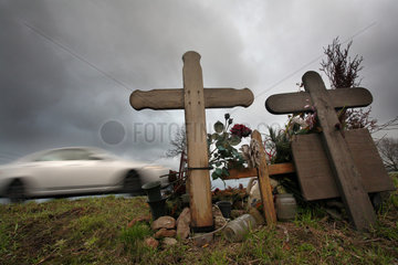 Holzkreuze zur Erinnerung an Unfallopfer und vorbeifahrendes Auto
