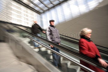 Aeltere Menschen fahren auf einer Rolltreppe hinab