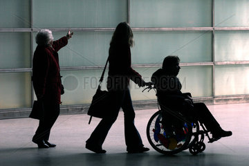 Silhouette einer Frau im Rollstuhl und ihrer Begleitung