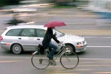 Frau mit Schirm auf dem Fahrrad im Stadtverkehr