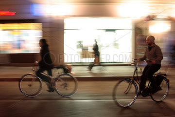 Fahrradfahrer nachts vor beleuchteten Schaufenstern