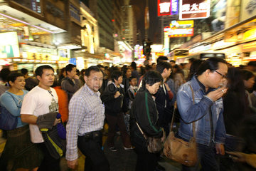 Passanten ueberqueren eine Strasse im Stadtteil Kowloon in Hongkong