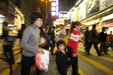 Frauen mit Kind ueberqueren eine Strasse im Stadtteil Kowloon in Hongkong