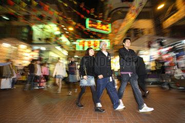 Junge Menschen in einer Geschaeftsstrasse im Stadtteil Kowloon in Hongkong