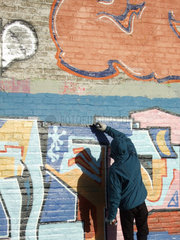 Berlin  Deutschland  Jugendlicher in Kapuzenjacke sprueht ein Graffito an eine Wand