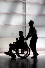 Silhouetten einer im Rollstuhl sitzenden Seniorin und ihrem Betreuer