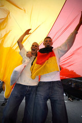 Berlin  Fussballfans WM 2006: Jubelnder Jugendliche unter riesiger Deutschlandflagge