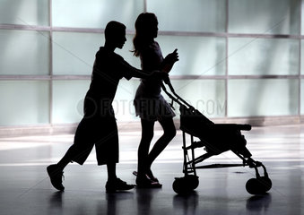 Silhouetten eines Maedchens und eines Jungen mit Kinderwagen