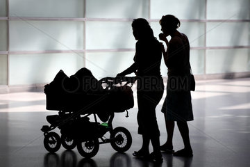 Silhouetten zweier junger Frauen mit einem Kinderwagen fuer Zwillinge
