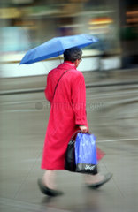 Rentnerin mit Regenschirm und Einkaufstuete