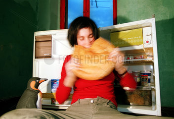 Frau isst gierig Brot vor geoeffnetem Kuehlschrank