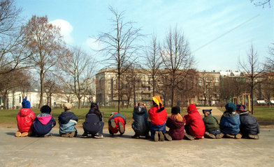Kinder einer Kita sitzen in einer Reihe im Freien