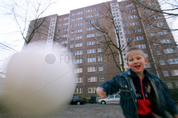 Ein Junge spielt Ball vor einem Hochhaus in Berlin