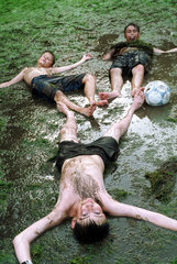 Drei Jungen liegen nach einem Fussballspiel im Schlamm