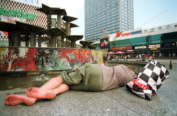 Obdachloser Mann schlaeft an einem Brunnen in Berlin