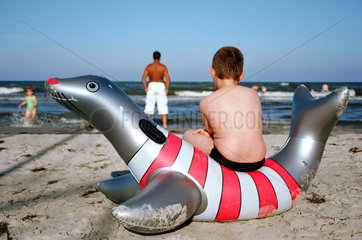 Junge sitzt auf Gummitier am Strand an der Ostsee