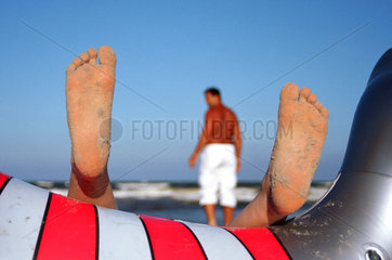 Fuesse eines Kindes auf Gummitier u. Vater am Strand