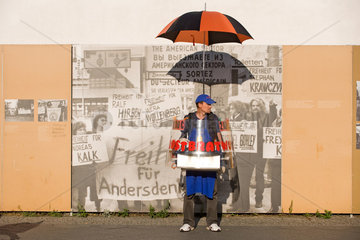 Berlin  Deutschland  ein Wurstverkaeufer vor einem Bild der DDR am Checkpoint Charlie